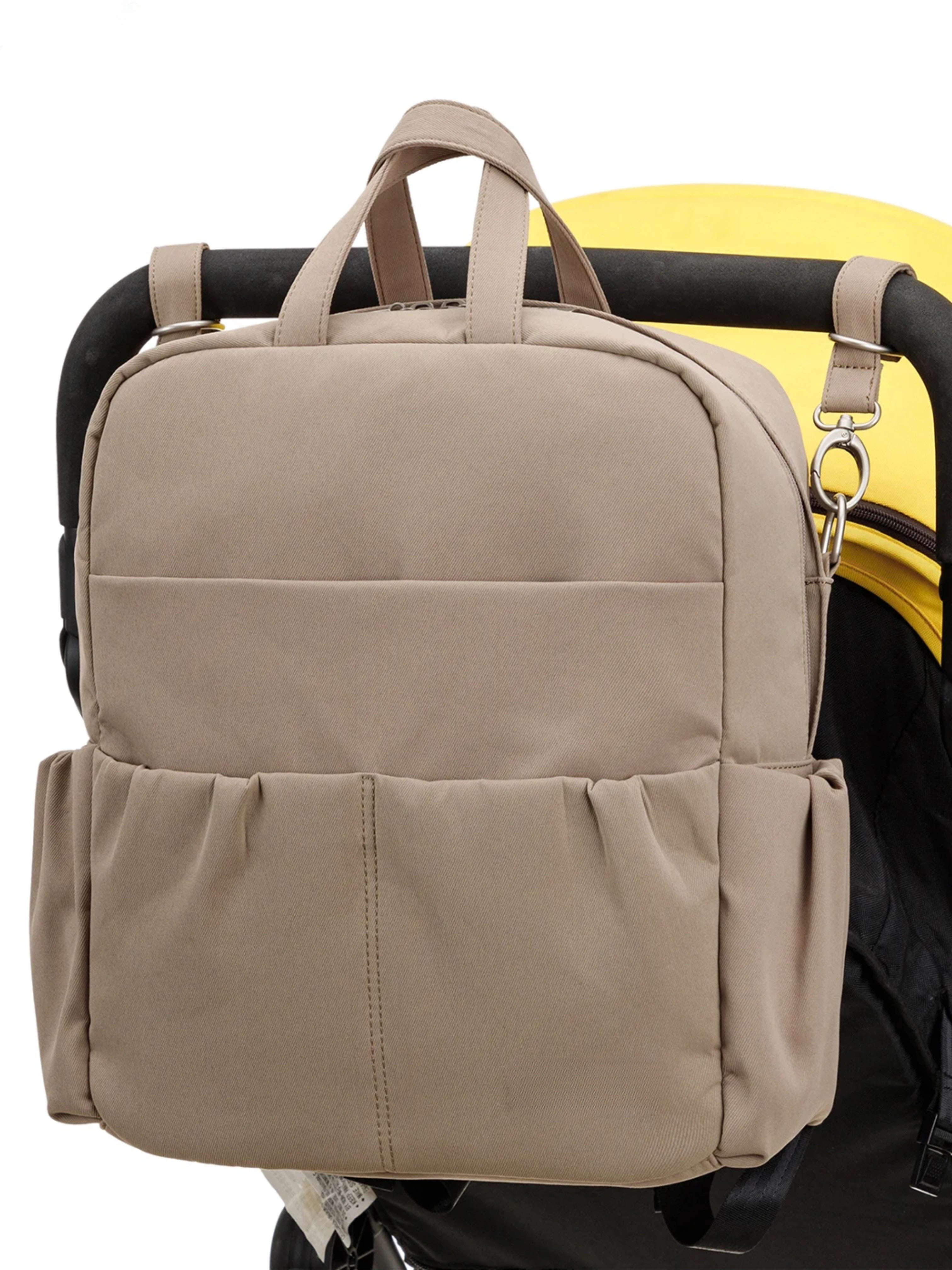 Sac à langer beige multifonction attaché à une poussette, avec plusieurs compartiments pratiques pour les affaires de bébé.