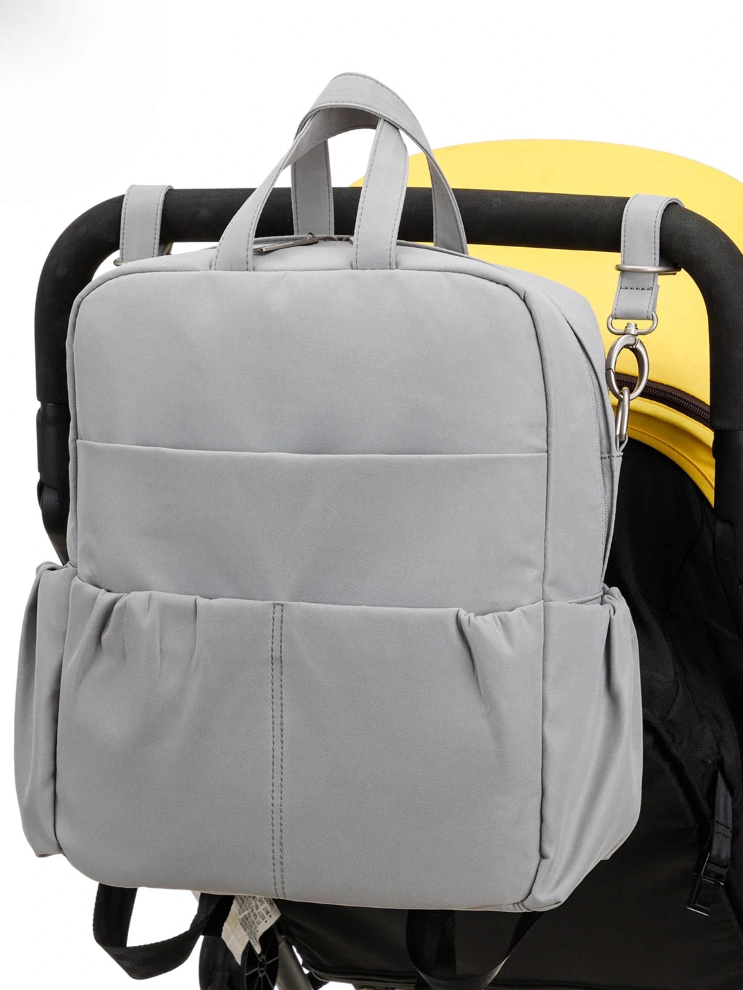 Sac à langer gris multifonction attaché à une poussette, avec poches latérales pour une organisation optimale des affaires de bébé.