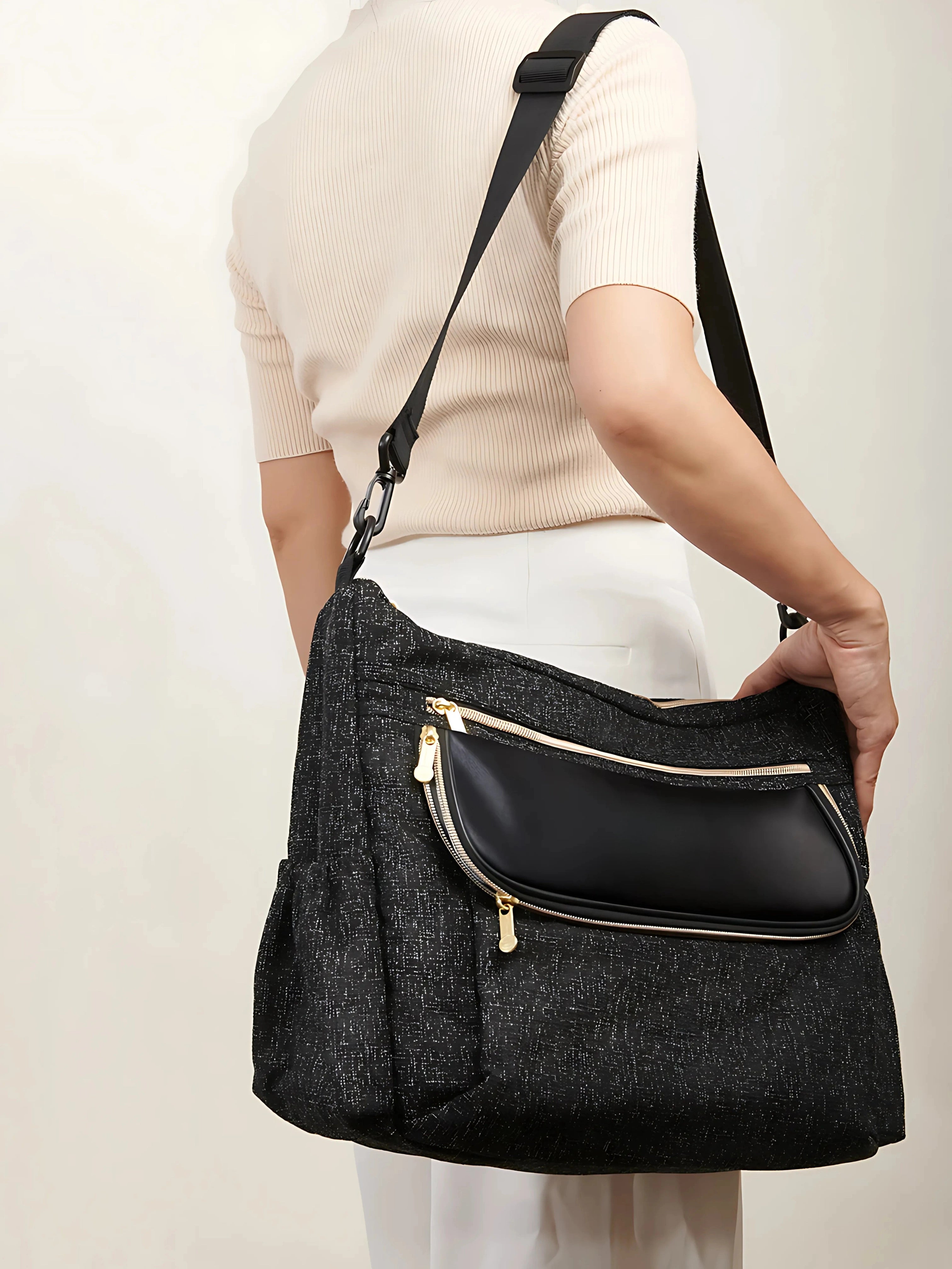 Sac à langer noir porté à l’épaule avec une bandoulière réglable, design pratique et élégant pour les sorties avec bébé.