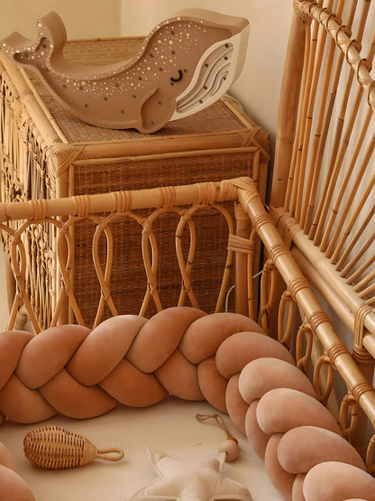 Tresse de lit bébé terracotta dans un berceau en rotin, avec décoration naturelle et jouets en bois.