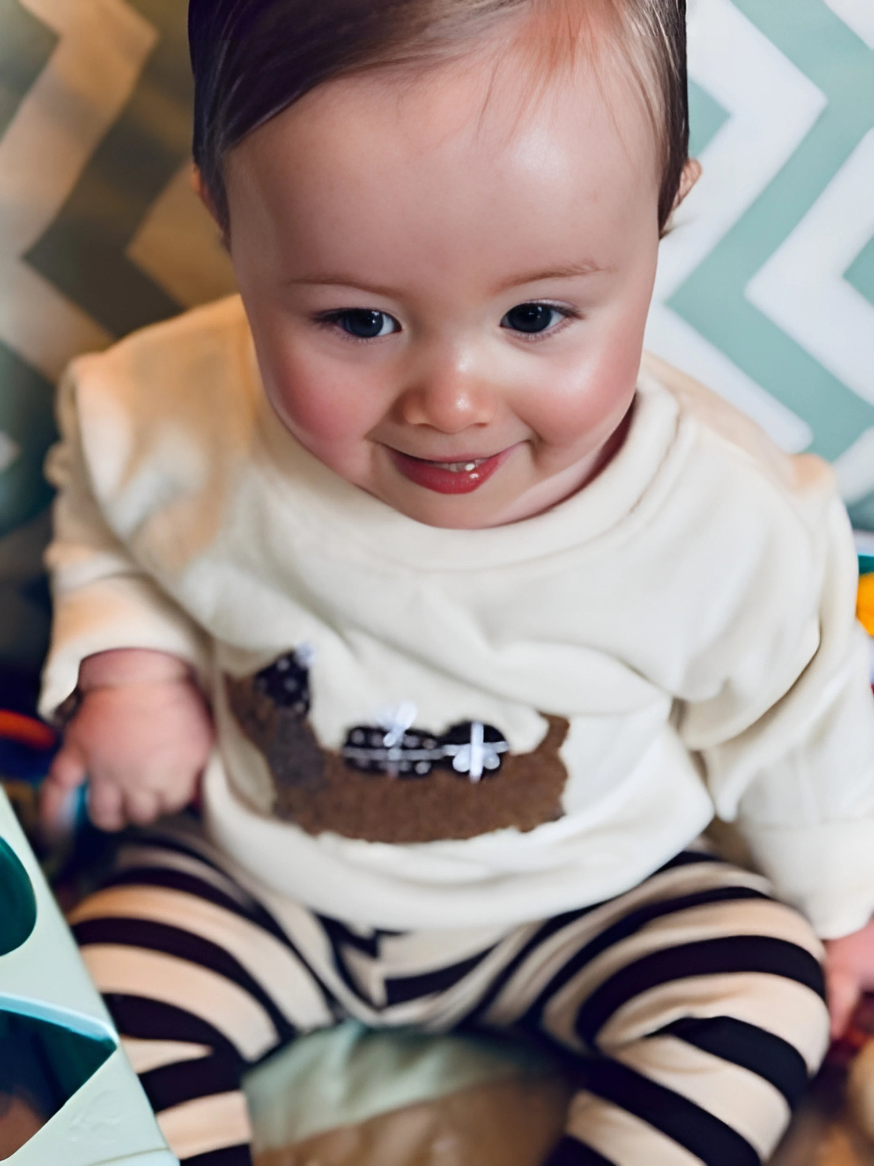 Bébé souriant dans une tenue confortable et élégante, avec un pull brodé et un legging rayé. Une tenue idéale pour les journées cocooning.